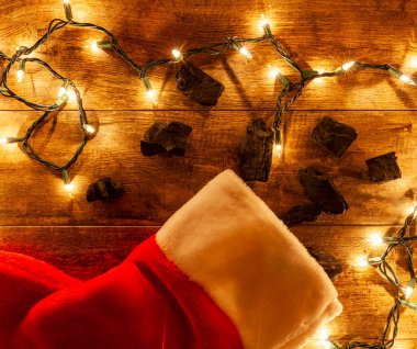 Terbiyesiz çocuk Noel konsepti için kömür alıyor. Kömür parçaları Noel çorabından çıkartılır. Ahşap arka planda sicim ışıkları olur..