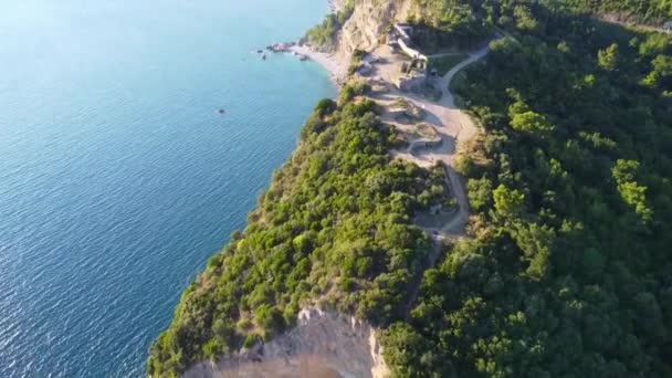 モンテネグロ、ブドヴァ、明るい日差しの下でターコイズブルーの海と緑豊かな森の間のモグレン要塞遺跡の空中ビュー — ストック動画