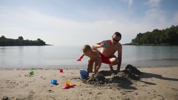 Πατέρας και κόρη χτίζουν κάστρο άμμου στην παραλία την ηλιόλουστη μέρα. — Αρχείο Βίντεο