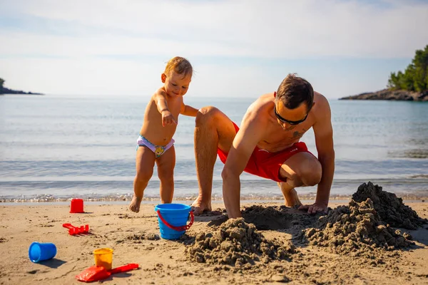 Padre e hija construyendo castillo de arena en la playa en un día soleado. — Foto de Stock