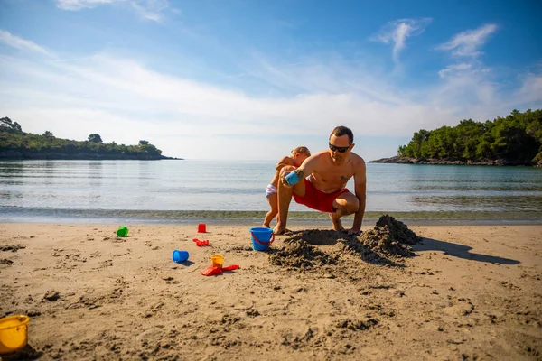 Padre e hija construyendo castillo de arena en la playa en un día soleado. — Foto de Stock