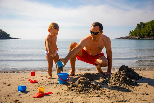 Padre e hija construyendo castillo de arena en la playa en un día soleado. — Foto de Stock