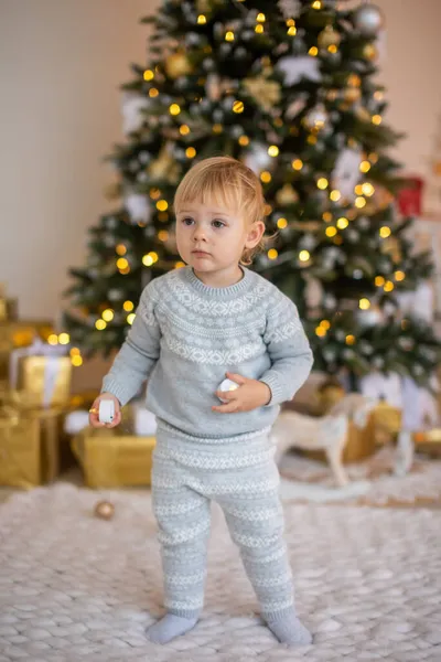 Adorable petite fille assise près du sapin de Noël avec des lumières festives et des cadeaux de Noël. Noël et Nouvel An. — Photo