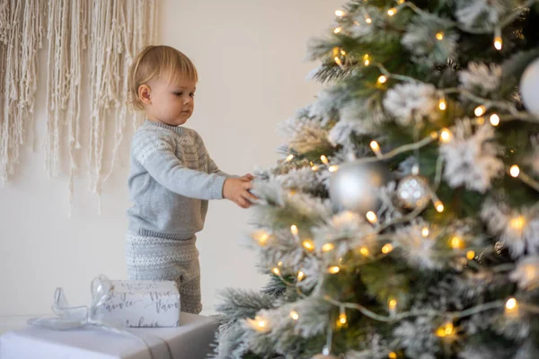 Adorable petite fille assise près du sapin de Noël avec des lumières festives et des cadeaux de Noël. Noël et Nouvel An. — Photo