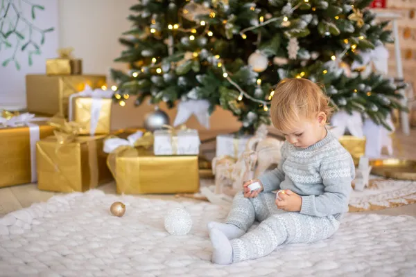 Menina adorável sentada perto da árvore de Natal com luzes festivas e presentes de xmas. Chrismas e Ano Novo. — Fotografia de Stock