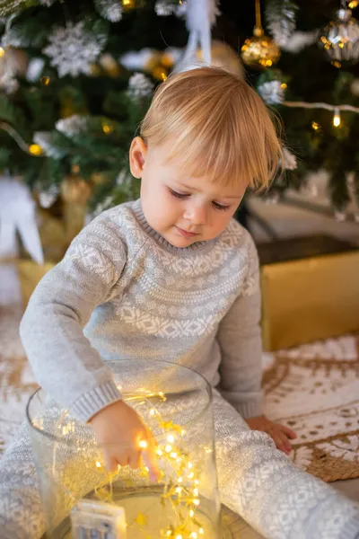 Adorable petite fille assise près du sapin de Noël avec des lumières festives et des cadeaux de Noël. Noël et Nouvel An. — Photo