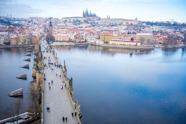 Lidé chodí po Karlově mostě, jehož střechy jsou v zimě pokryty sněhem, v Praze — Stock fotografie
