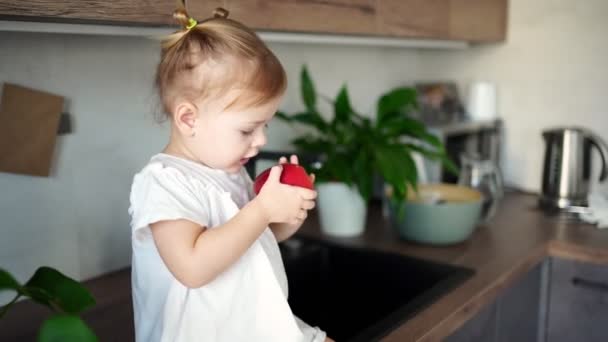 Baby girl blondýnka jíst jablko v kuchyni, koncept zdravé jídlo pro děti — Stock video