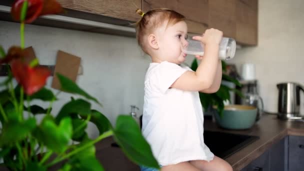 快乐的女婴坐在厨房的桌子边，喝牛奶 — 图库视频影像