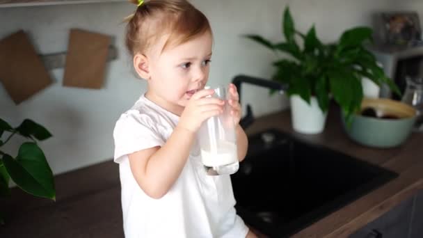 Glückliches kleines Mädchen sitzt am Tisch in der Küche und trinkt Milch — Stockvideo