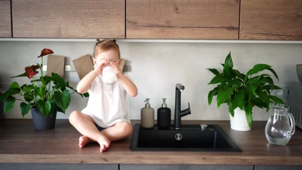 Mutfaktaki masada oturup süt içen mutlu bir kız bebek. — Stok video