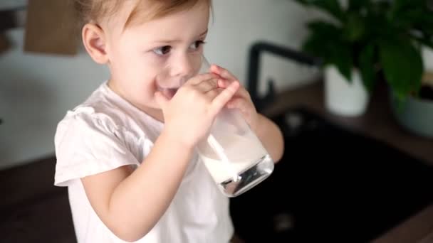 Mutfaktaki masada oturup süt içen mutlu bir kız bebek. — Stok video