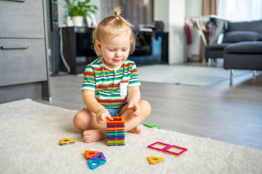 Evde renkli mıknatıs blokları seti oynayan küçük bir kız. Eğitici oyunlar oynayan çocuk. Erken çocukluk gelişimi.