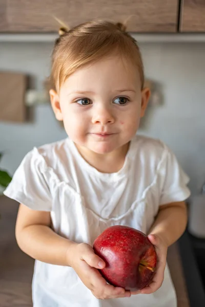 Niña rubia comiendo una manzana en la cocina, concepto de comida saludable para niños —  Fotos de Stock