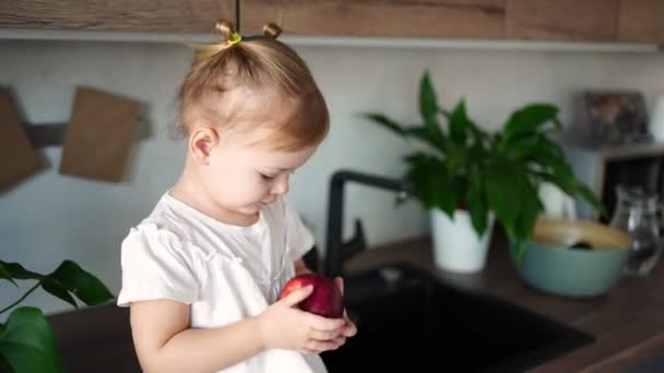 Blondes Mädchen isst einen Apfel in der Küche, Konzept der gesunden Ernährung für Kinder — Stockvideo