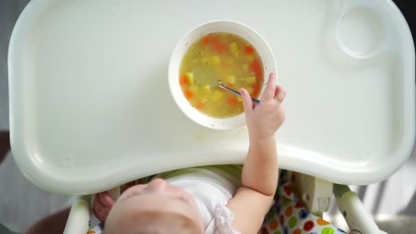 Sevimli bebek bebek yüksek sandalyede oturuyor ve evde yemek çorbasını içiyor.. — Stok video