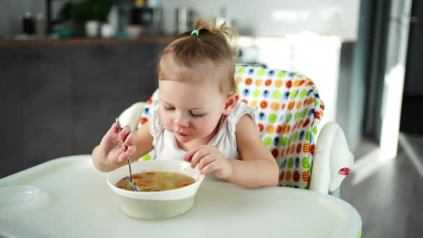 Roztomilé dítě dívka batole sedí na vysoké židli a jí oběd polévka doma kuchyně. — Stock video