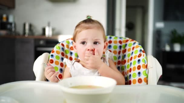 Cute baby girl maluch siedzi na wysokim krześle i jedzenie jej zupy lunchowej w domu kuchnia. — Wideo stockowe