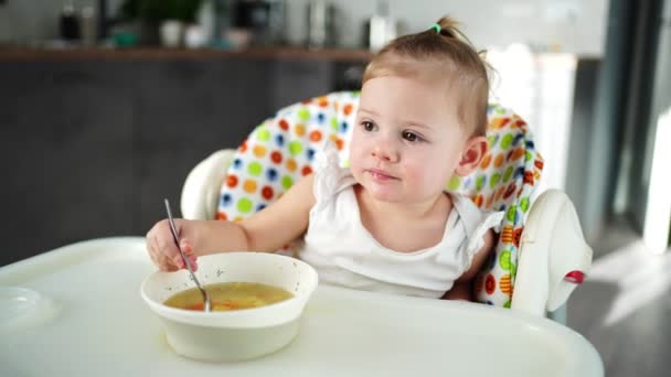 Roztomilé dítě dívka batole sedí na vysoké židli a jí oběd polévka doma kuchyně. — Stock video