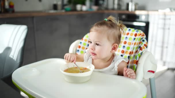 Roztomilé dítě dívka batole sedí na vysoké židli a jí oběd polévka doma kuchyně. — Stock video
