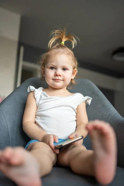 Sorridente bambina è seduta sulla poltrona e utilizzando smart phone — Foto Stock