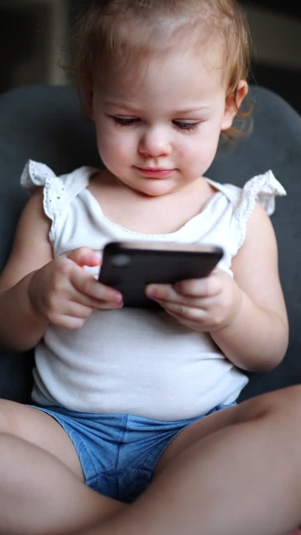 Sorridente bambina è seduta sulla poltrona e utilizzando smart phone — Video Stock