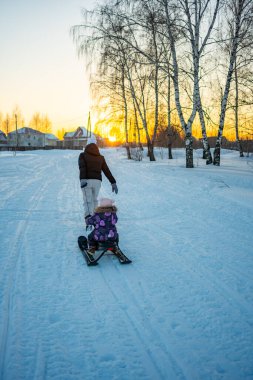Küçük çocukla birlikte karlı arazide plastik kızak çeken genç bir kadın. Kış doğası. Aile.