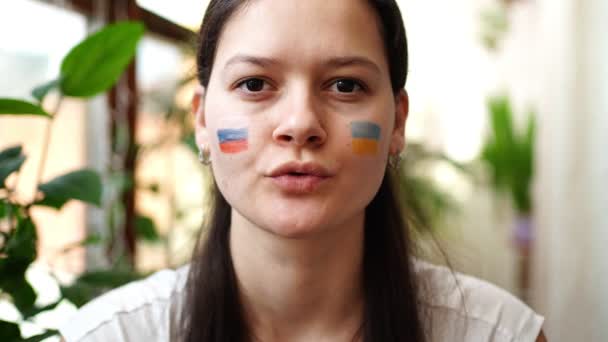 Młoda rosyjsko-ukraińska dziewczyna z flagą Ukrainy i Rosji na twarzy mówi STOP WAR. Koncepcja udziału narodu ukraińskiego w wojnie z Rosją. Nie pojęcie wojny.. — Wideo stockowe