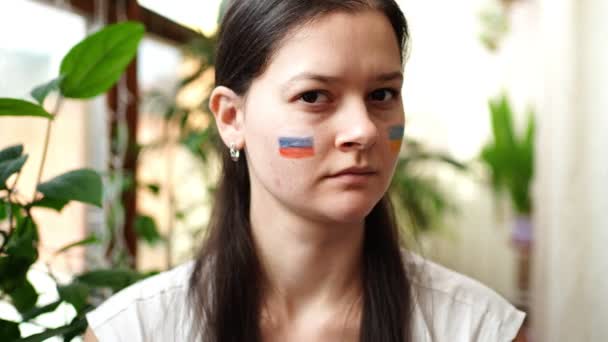 Smutná mladá rusko-ukrajinská dívka s vlajkou Ukrajiny a Ruska na tváři třese hlavou NE. Koncept účasti ukrajinského lidu ve válce s Ruskem. Ne válečný koncept — Stock video