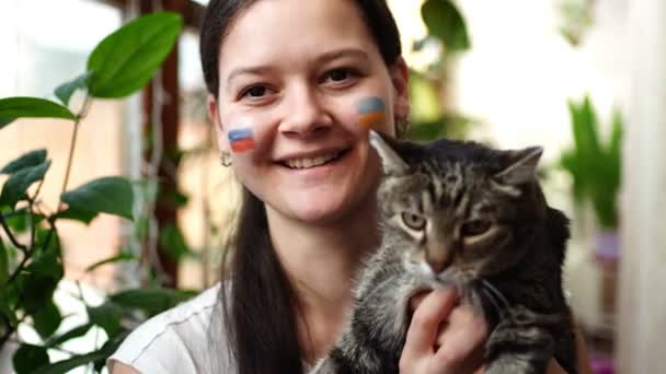 Uśmiecha się młoda rosyjsko-ukraińska dziewczyna z flagą Ukrainy i Rosji na twarzy. Koncepcja udziału narodu ukraińskiego w wojnie z Rosją. Nie pojęcie wojny. — Wideo stockowe