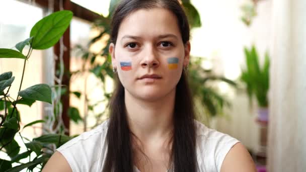 Молодая русско-украинская девушка с флагом Украины и России на лице говорит "Стоп". Концепция участия украинского народа в войне с Россией. Не военное понятие. — стоковое видео