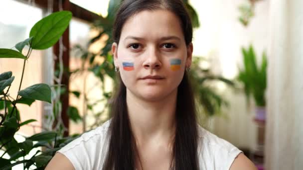 Jeune fille russo-ukrainienne avec le drapeau de l'Ukraine et la Russie sur son visage montre cœur par les mains. Le concept de participation du peuple ukrainien à la guerre contre la Russie. Pas concept de guerre — Video