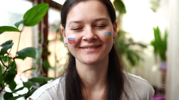 Une jeune fille russo-ukrainienne avec le drapeau de l'Ukraine et de la Russie sur le visage sourit. Le concept de participation du peuple ukrainien à la guerre contre la Russie. Pas concept de guerre — Video