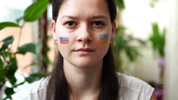 Seorang gadis muda Rusia-Ukraina dengan bendera Ukraina dan Rusia di wajahnya menunjukkan diam. Konsep partisipasi rakyat Ukraina dalam perang dengan Rusia. Bukan konsep perang. — Stok Video