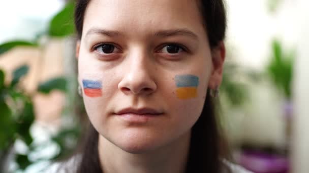 Ein trauriges junges russisch-ukrainisches Mädchen mit der Flagge der Ukraine und Russlands auf dem Gesicht schüttelt den Kopf NEIN. Das Konzept der Beteiligung des ukrainischen Volkes am Krieg gegen Russland. Kein Kriegskonzept — Stockvideo