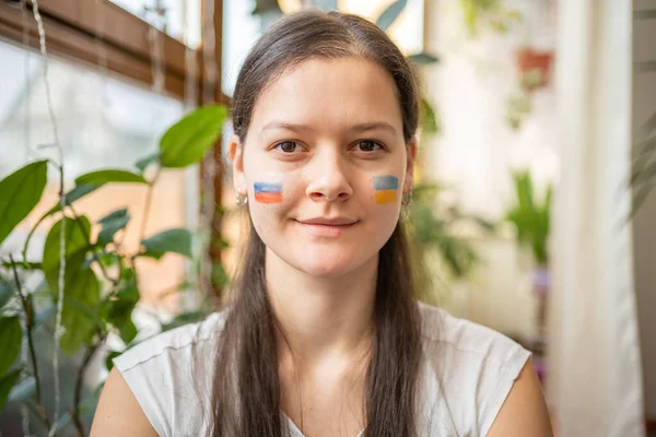 Portrait of young Russian-Ukrainian girl with the flag of Ukraine and Russia on her face. The concept of participation of the Ukrainian people in the war with Russia. Not war concept
