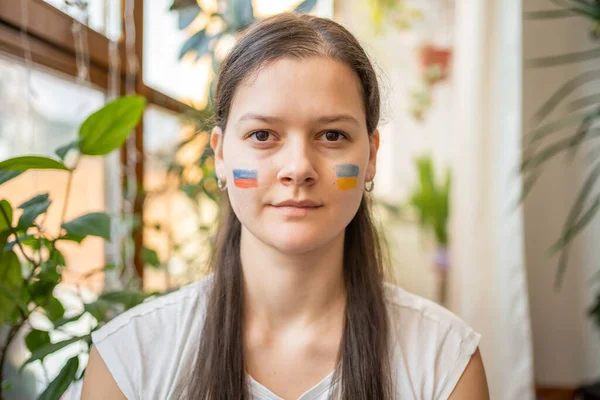 Portrait of young Russian-Ukrainian girl with the flag of Ukraine and Russia on her face. The concept of participation of the Ukrainian people in the war with Russia. Not war concept