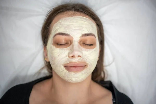 Beautiful happy woman in the spa making face mask treatment. Beauty industry concept.