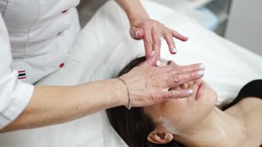 Yüz masajı. Güzellik kliniğinde kadın kozmetik uzmanı tarafından yüz temizleme ameliyatındaki kadın portresi. Güzellik endüstrisi konsepti. 