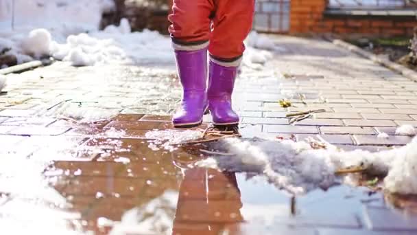 Child jumps on puddles in rubber boots at sunset lights in spring time — ストック動画