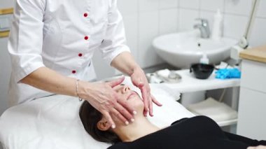 Yüz masajı. Güzellik kliniğinde kadın kozmetik uzmanı tarafından yüz temizleme ameliyatındaki kadın portresi. Güzellik endüstrisi konsepti. 