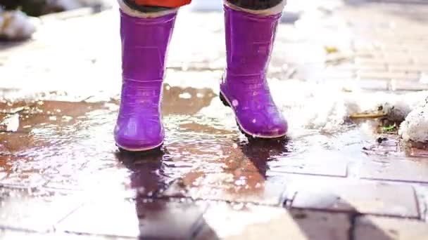 Child jumps on puddles in rubber boots at sunset lights in spring time — ストック動画