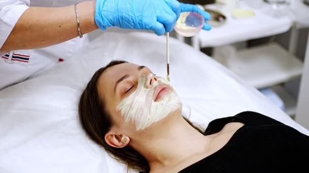 Médecin cosmétologue ou dermatologue faisant masque facial dans le salon de cosmétologie. Esthéticienne professionnelle appliquant un masque facial sur un visage de femme caucasienne couché sur un lit en peignoir. — Video