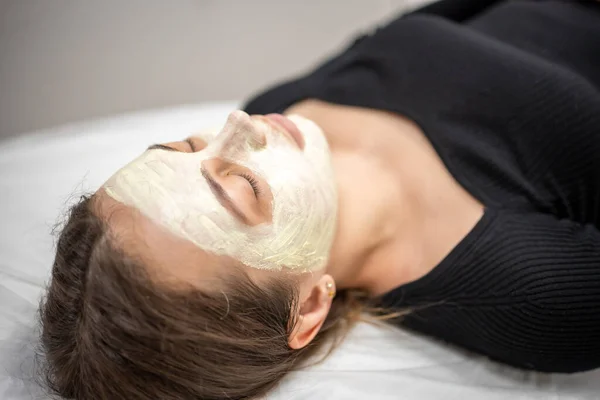 Beautiful happy woman in the spa making face mask treatment. Beauty industry concept.