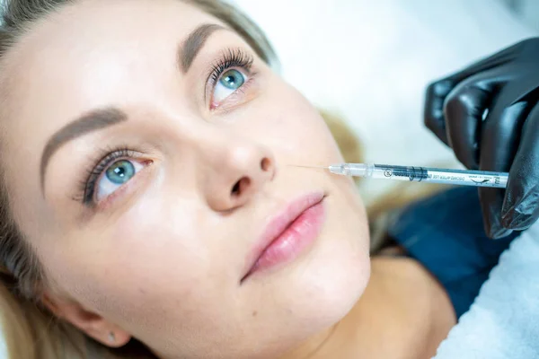 Close-up of woman face and hand in surgical glove holding syringe near her lips, ready to receive beauty treatment. Injection cosmetology, aesthetic surgery
