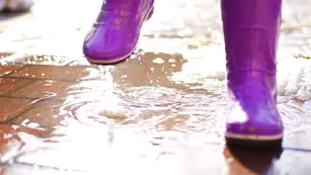 Niño salta sobre charcos en botas de goma al atardecer luces en primavera — Vídeos de Stock