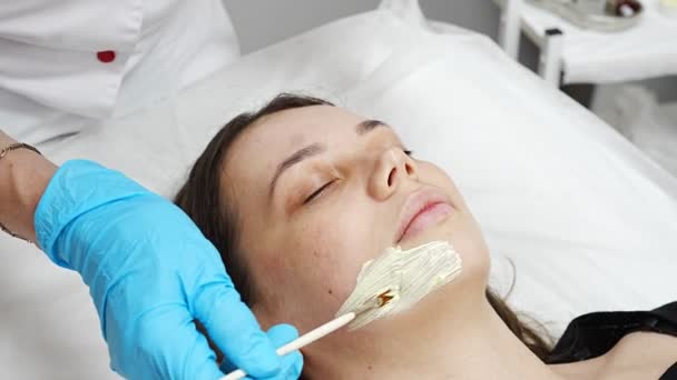 Médecin cosmétologue ou dermatologue faisant masque facial dans le salon de cosmétologie. Esthéticienne professionnelle appliquant un masque facial sur un visage de femme caucasienne couché sur un lit en peignoir. — Video
