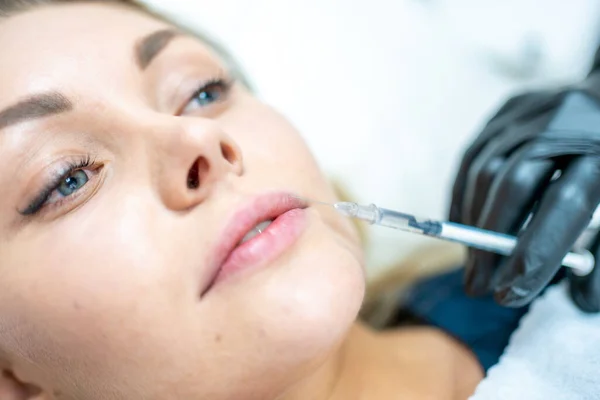 Close-up of woman face and hand in surgical glove holding syringe near her lips, ready to receive beauty treatment. Injection cosmetology, lips augmentation and correction concept.