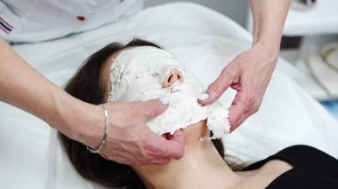 Doktor kozmetolog ya da dermatolog kozmetoloji salonunda yüz maskesi yapıyor. Profesyonel Güzellik Uzmanı, beyaz kadın yüzüne yüz maskesi takıyor. Yatakta bornozla yatıyor..