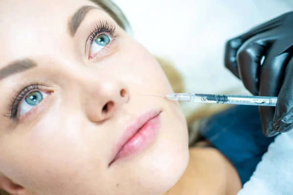 Close-up of woman face and hand in surgical glove holding syringe near her lips, ready to receive beauty treatment. Injection cosmetology, aesthetic surgery